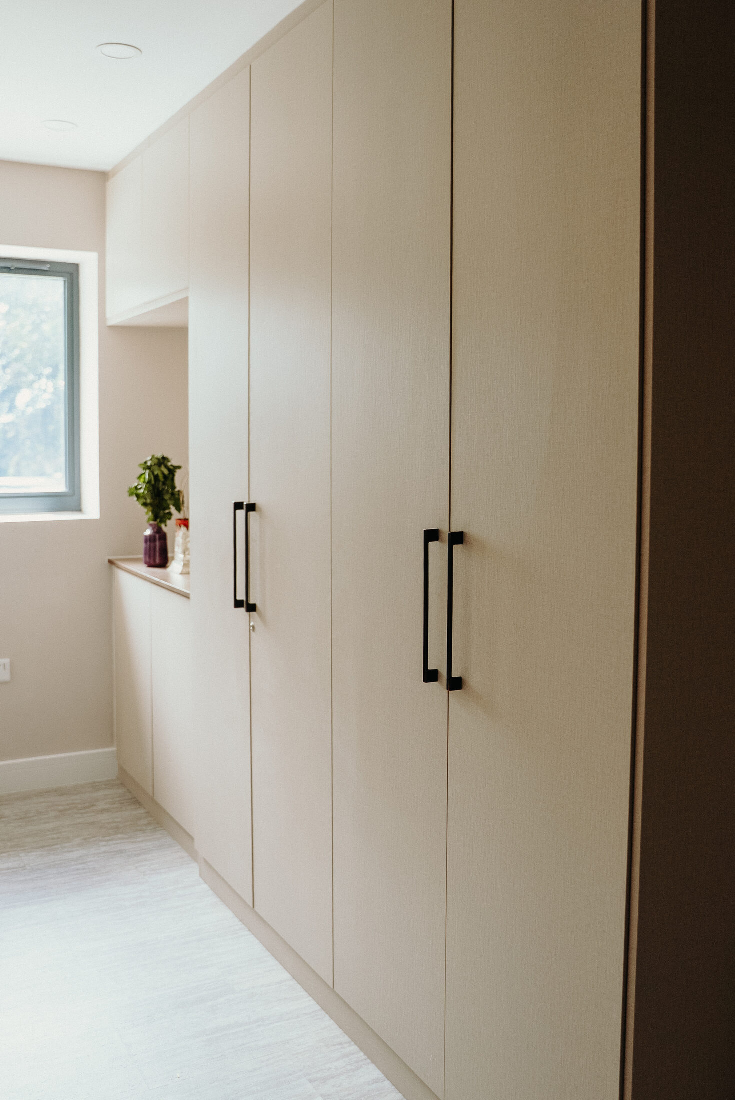 Run of cream fitted wardrobes with black handles by Sunny Interiors
