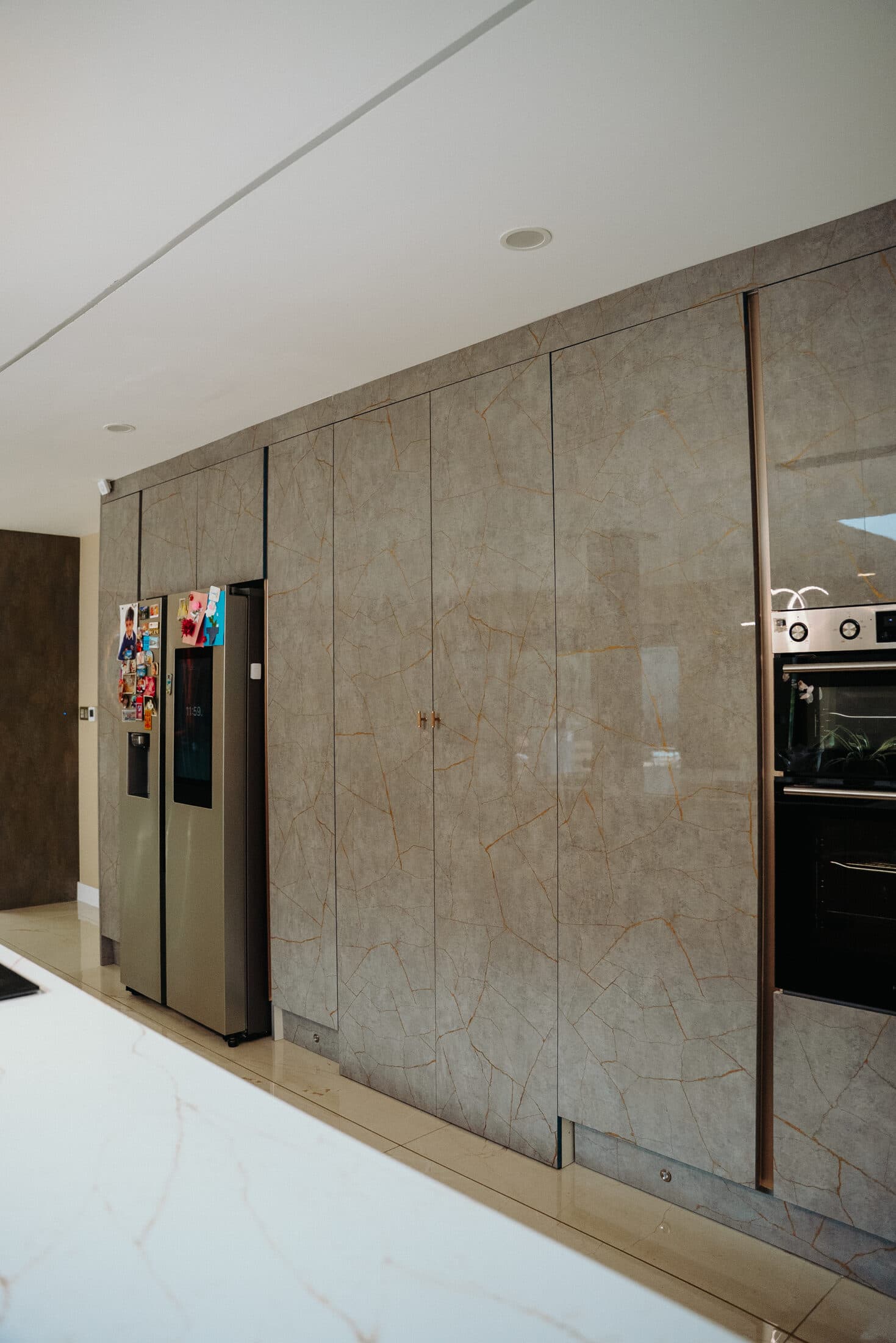 Grey marble effect floor to ceiling kitchen cabinet wall with integrated fridge by Sunny Interiors