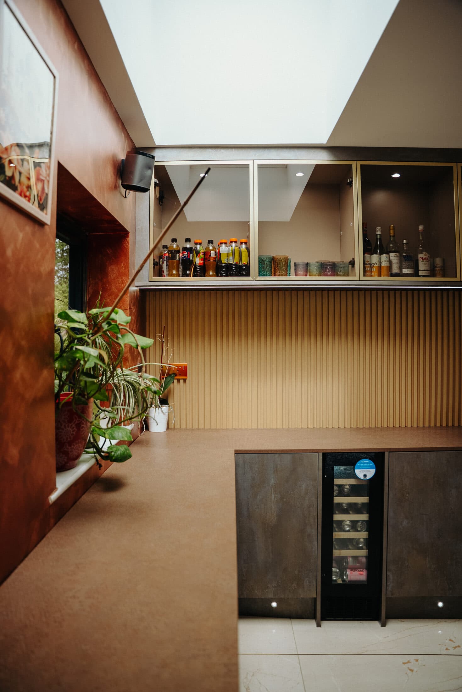 Home bar with copper coloured walls and glass fronted cabinets stocked with bottles and glasses by Sunny Interiors